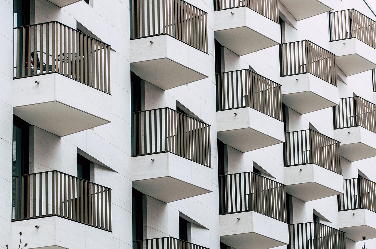 Façade blanche d'un immeuble moderne vue en biais, alignement de balcons aux garde-corps à barreaux noirs